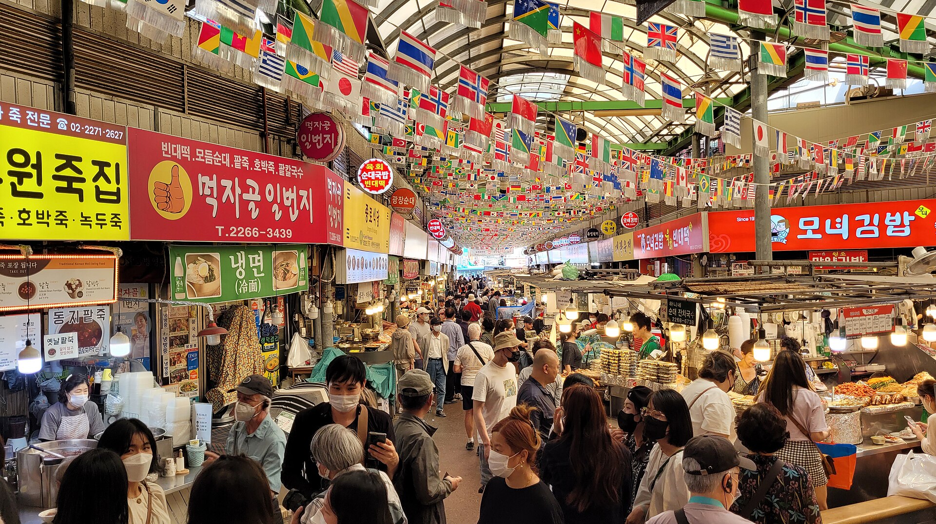 Crowded food alley under coloured flags at Gwangjang Market